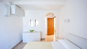A modern hotel room with a bed, a dresser, a mirror, and a hallway leading to another room.