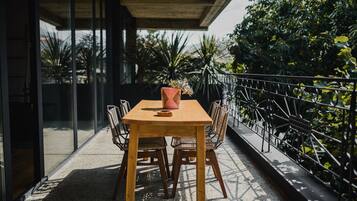 A wooden table with chairs on a balcony with a metal railing, surrounded by greenery.