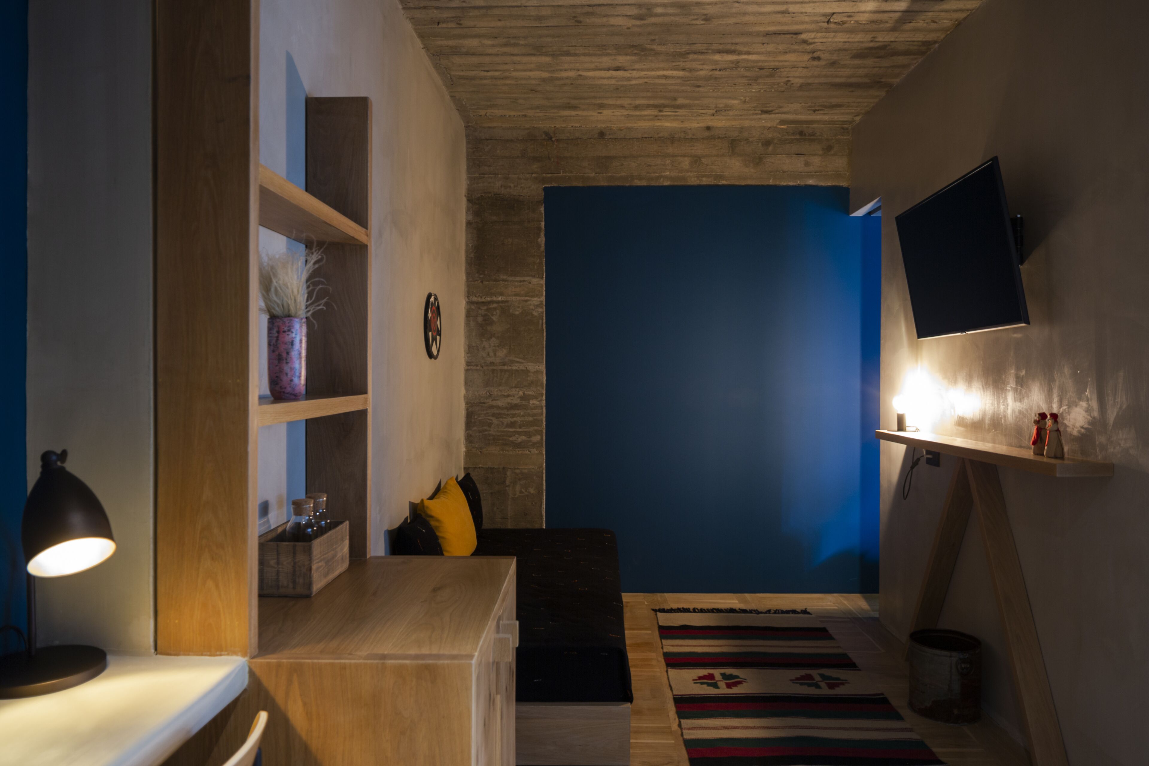 Um quarto acolhedor com uma escrivaninha de madeira, prateleiras, uma parede em azul e uma televisão na parede.