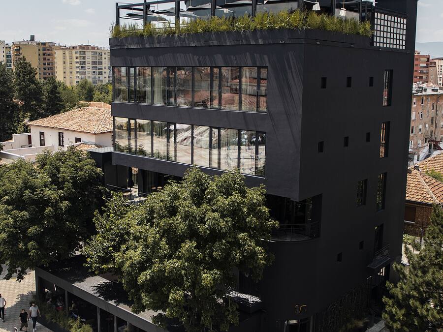 Ein modernes, mehrstöckiges Gebäude mit Dachgarten, großen Fenstern und einer flachen Dachterrasse.