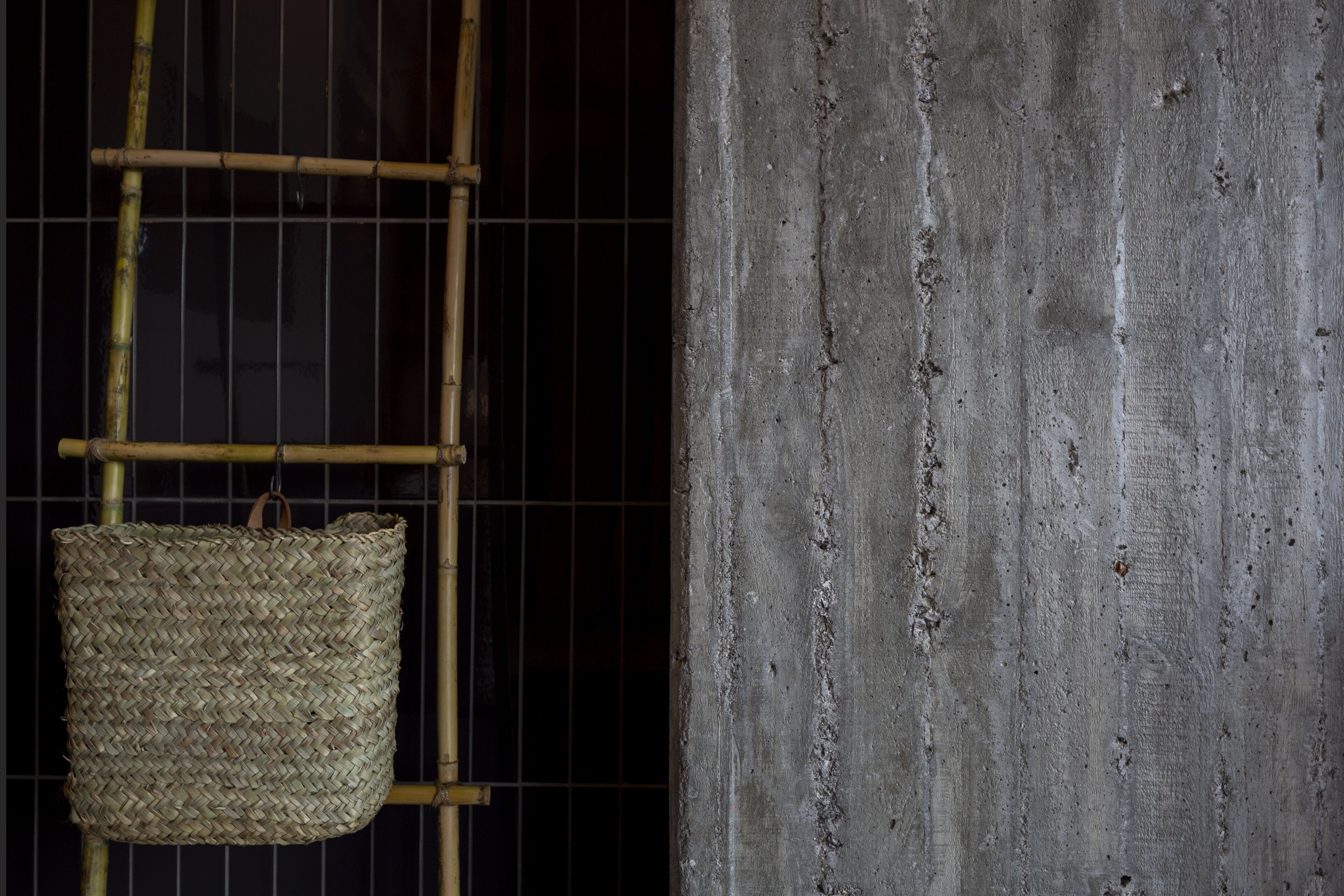 A bamboo ladder with a woven basket hanging from it, positioned against a dark background with a textured concrete wall.