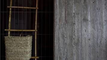 A bamboo ladder with a woven basket hanging from it, positioned against a dark background with a textured concrete wall.