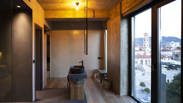 A modern interior with a minimalist design, featuring a wooden ceiling, a large window with a view of a cityscape, and a built-in sink on a wooden platform. - In Gallery Spa & Hotel (Korçë)