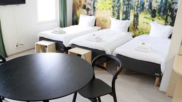 A hotel room with two beds, a round table, and a chair. - Hotelli Kuohu (Kangasala)
