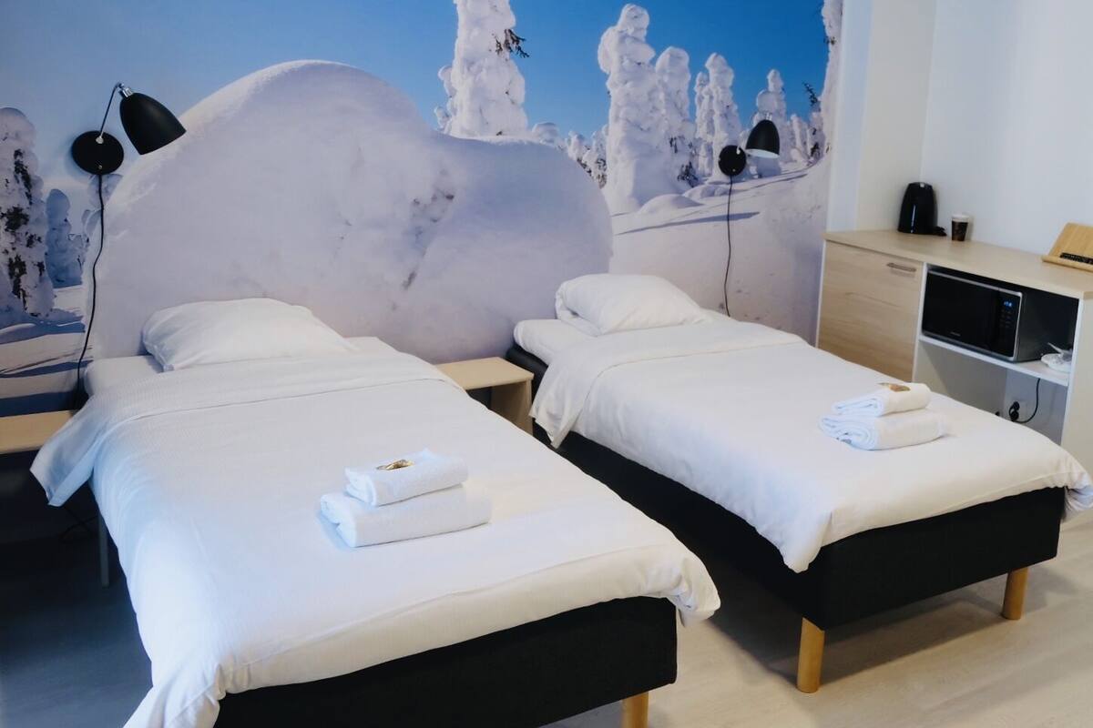 A hotel room with two beds, a nightstand, a desk, a microwave, and a wall with a snowy landscape mural.