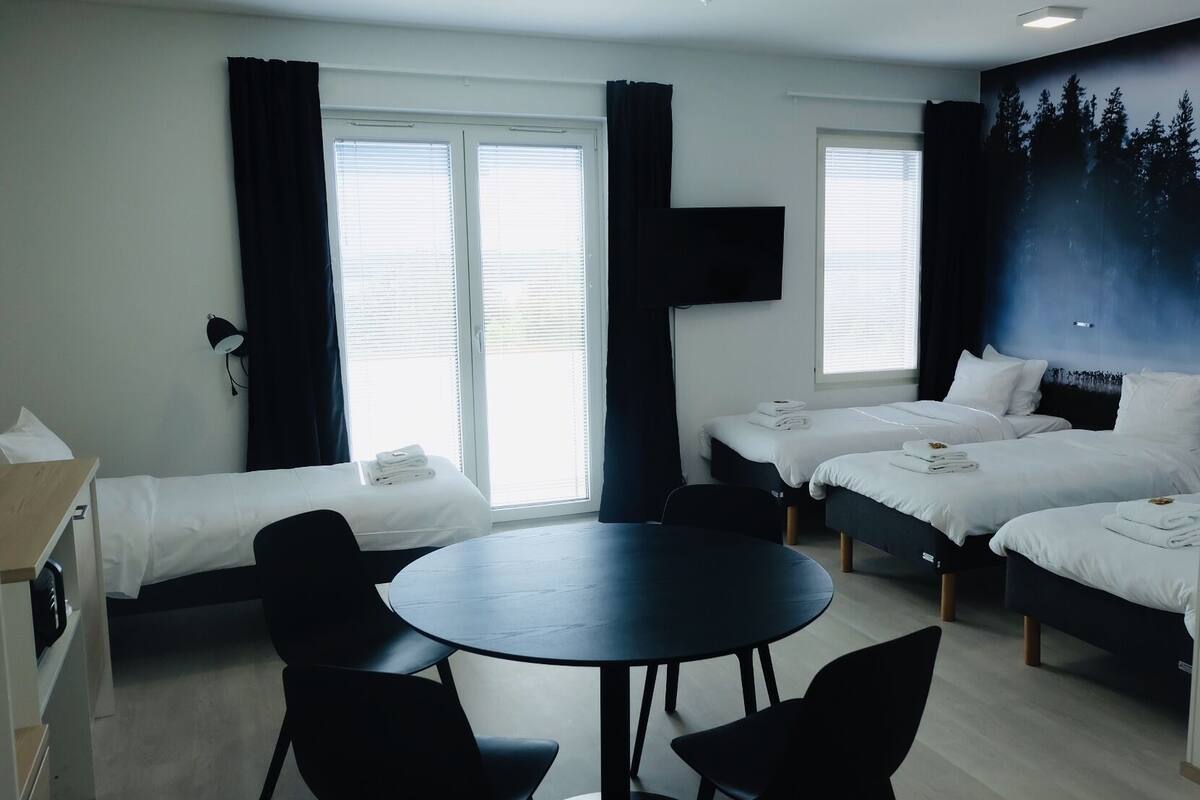 A hotel room with two single beds, a double bed, a round table, and two chairs.