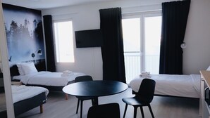 A hotel room with two beds, a round table, and chairs. There is a TV mounted on the wall, and a window with curtains. - Hotelli Kuohu (Kangasala)