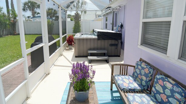 Een overdekt terras met een jacuzzi, een zithoek en een bloempot.