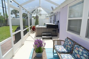 A covered patio with a hot tub, seating area, and a potted plant.