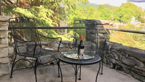 A patio with two metal chairs and a table, a bottle of wine, and a glass on the table. - The Castle - c. 1780 (Lexington)