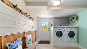 Une buanderie équipée de deux machines à laver, d’un banc avec des coussins et d’un mur en bois muni de crochets.