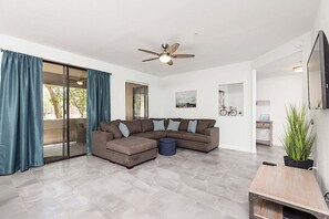 Una sala de estar con sofá modular, ventilador de techo, puerta corredera de vidrio y una mesita con una planta.