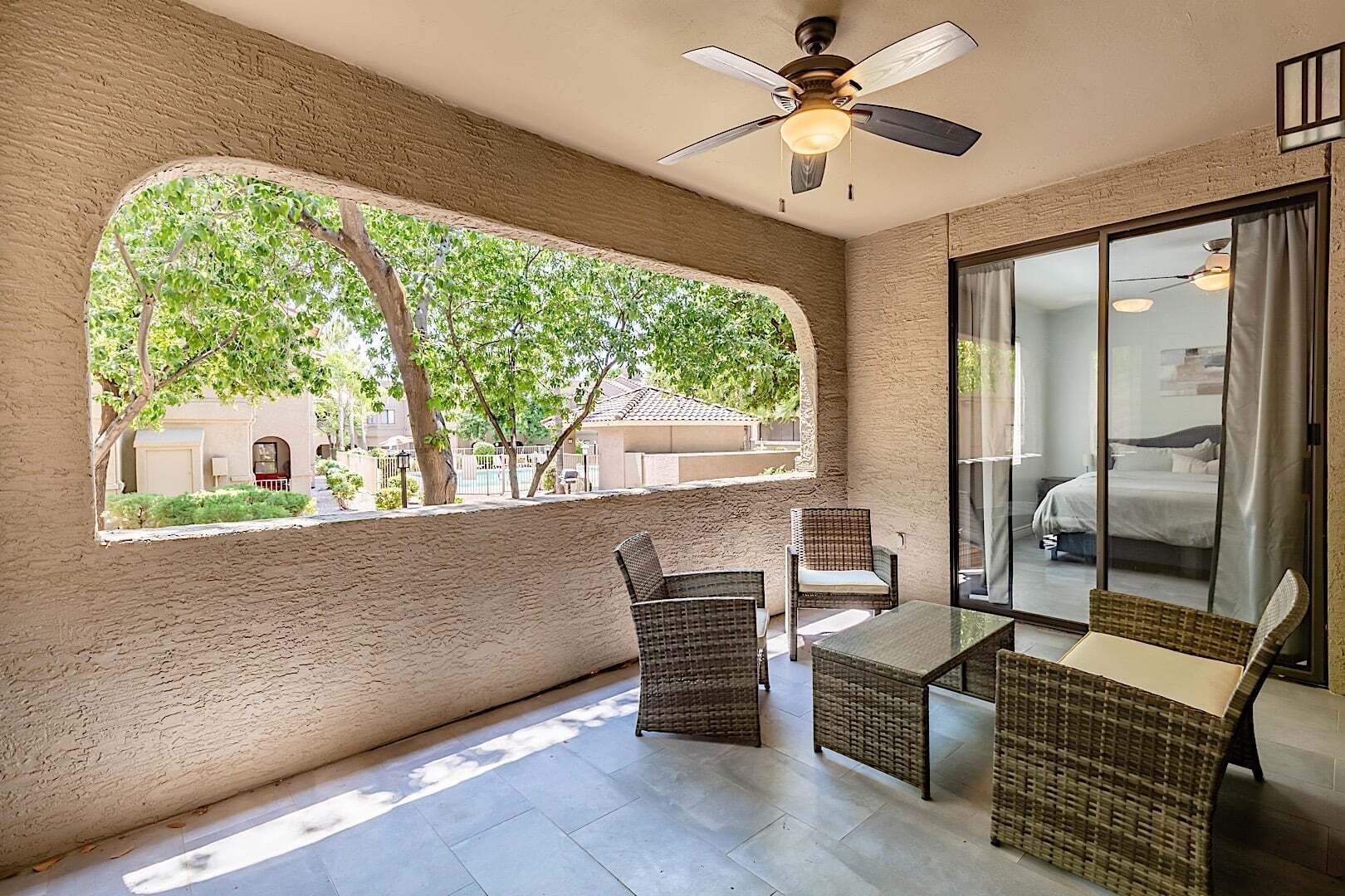 A room with a large window, wicker furniture, a ceiling fan, and a view of a residential area.