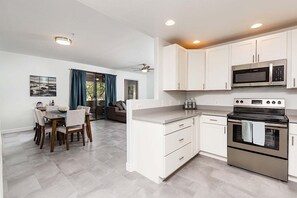 Una cocina moderna con gabinetes blancos, estufa de acero inoxidable y microondas.
