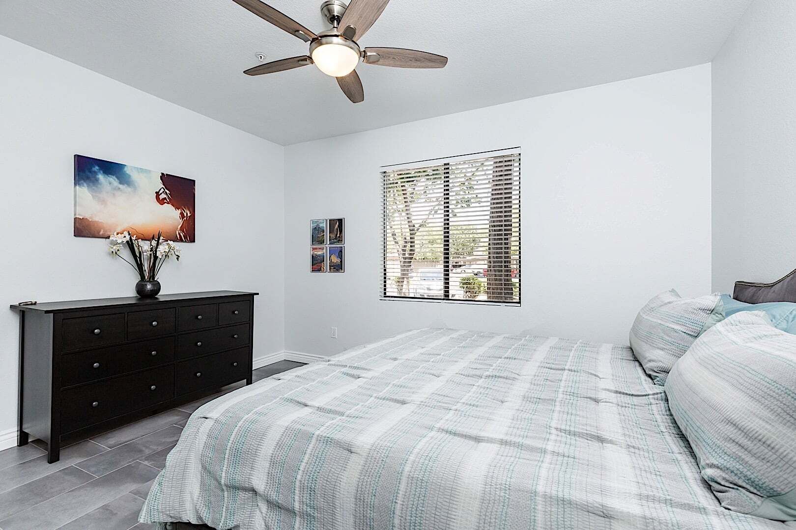 A bedroom with a bed, a dresser, a ceiling fan, and a window with blinds.