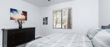 A bedroom with a bed, a dresser, a ceiling fan, and a window with blinds.