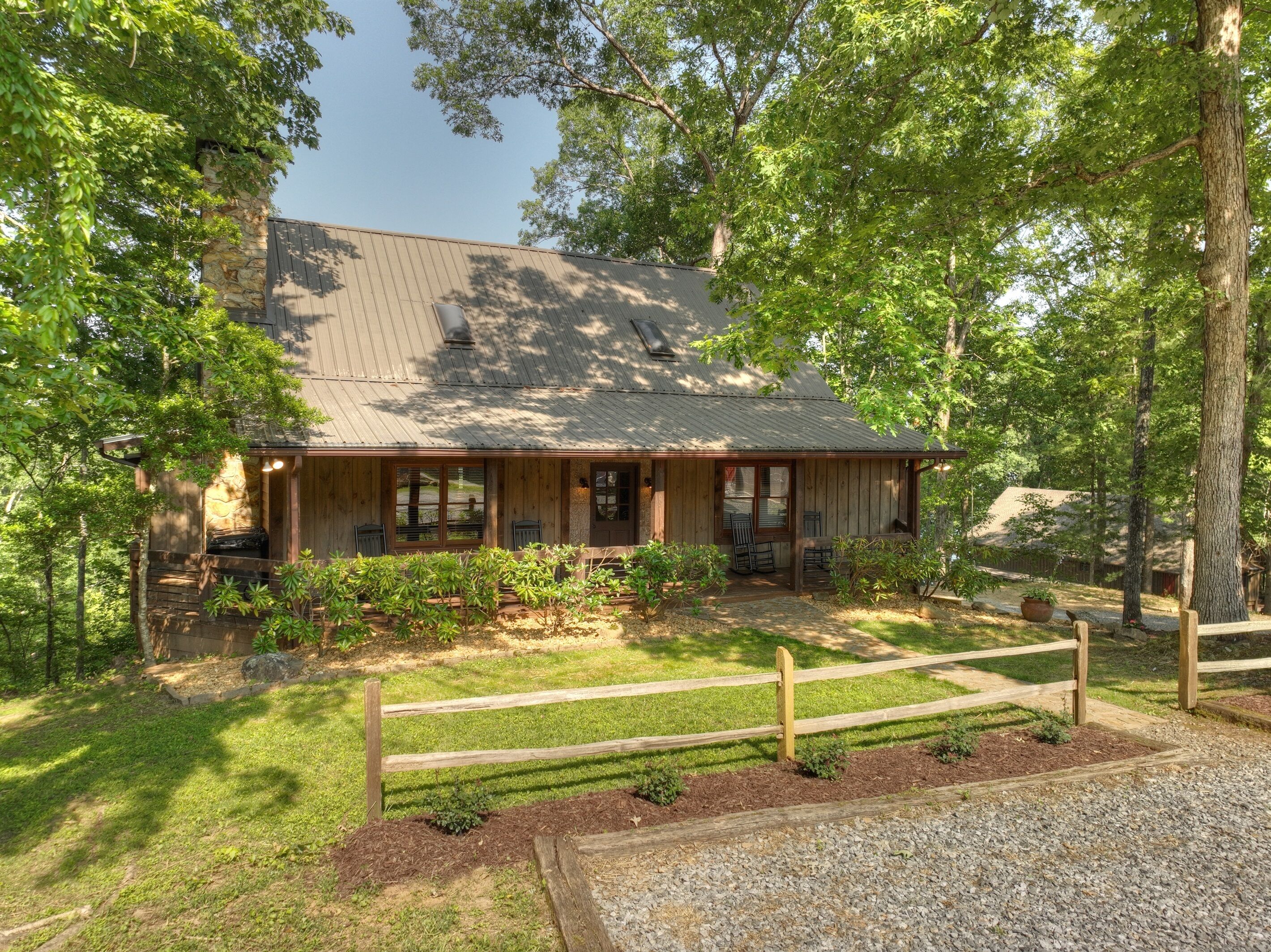 A rustic cabin with a stone foundation, wooden exterior, and a covered porch with seating.