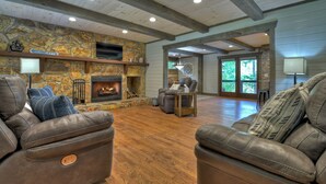 A spacious living room with a stone fireplace, leather sofas, and a wooden floor.