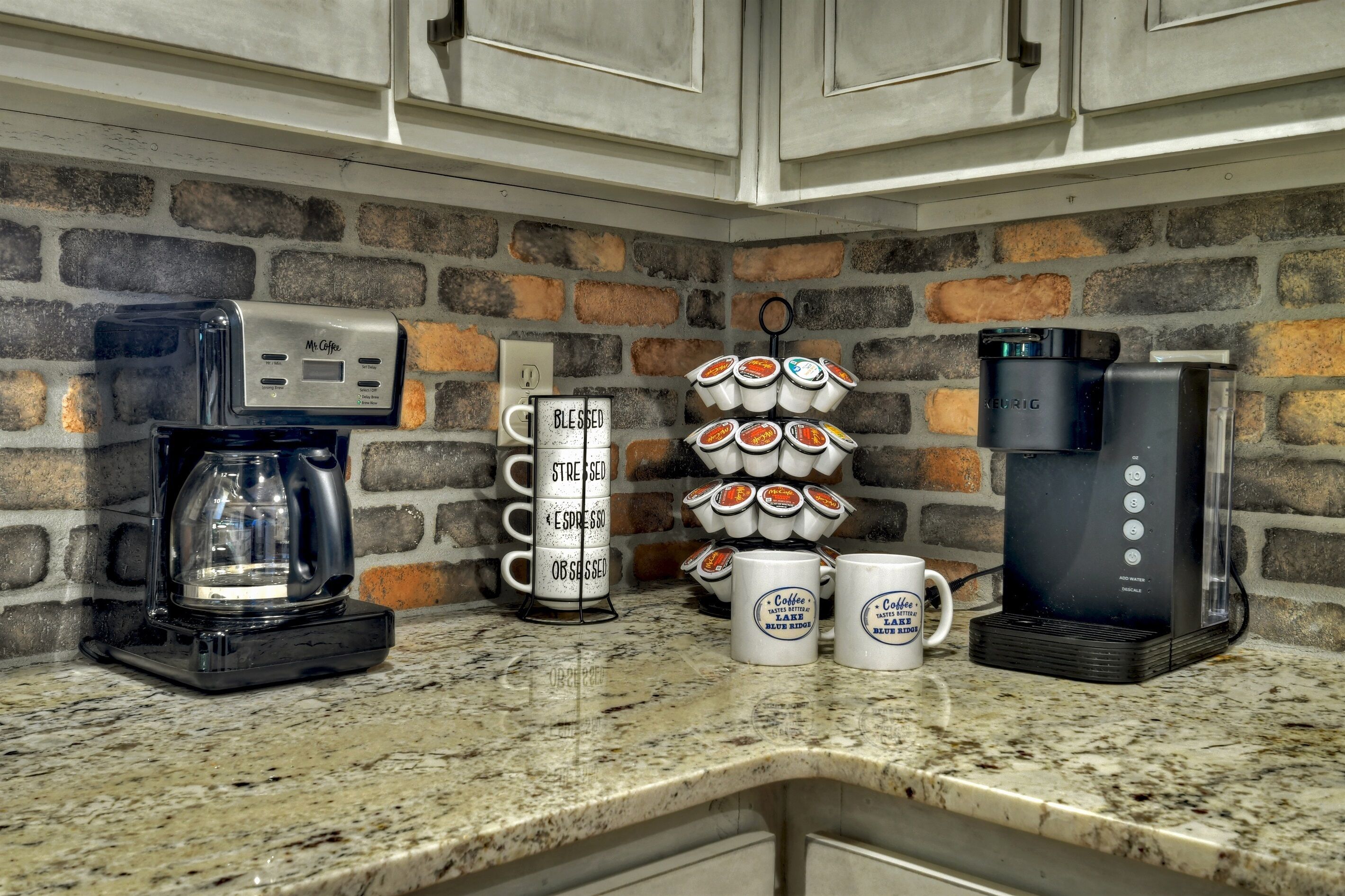 A kitchen counter with a coffee maker, a coffee station with mugs, and a coffee machine.