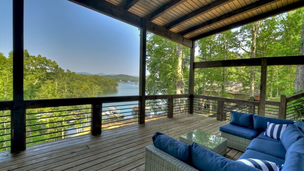 A covered outdoor deck with a view of a lake and forest.