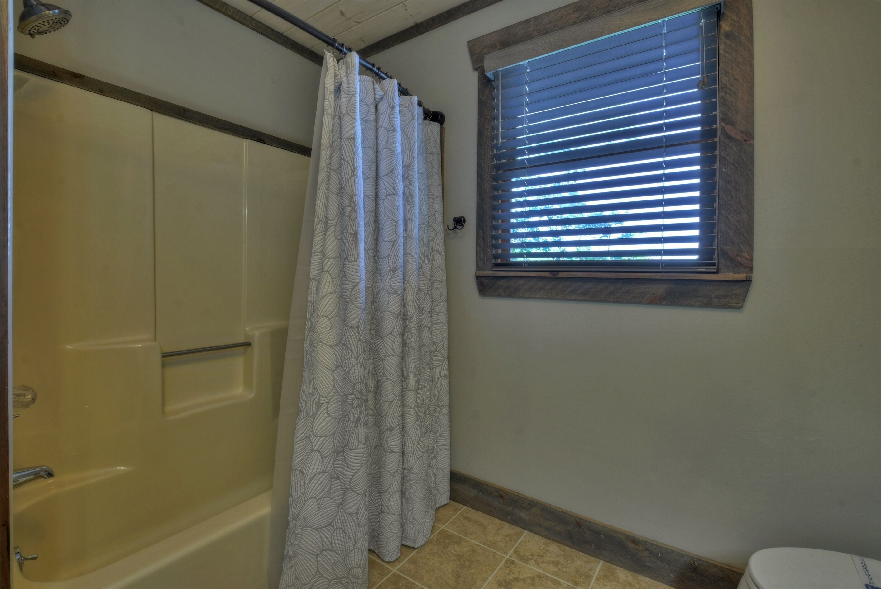 Une salle de bain avec douche, toilettes et fenêtre équipée de stores.