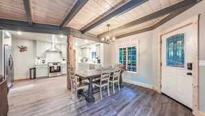 A spacious kitchen with modern appliances, a dining area with a wooden table and chairs, and a large window with a view. - The Sparrow’s Nest ~ Cozy Charm + Fire Pit Fun (Shaver Lake)