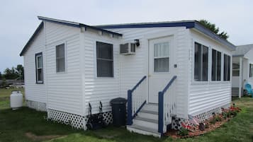 A small, single-story mobile home with a front porch, a small deck, and a front yard with a garden.
