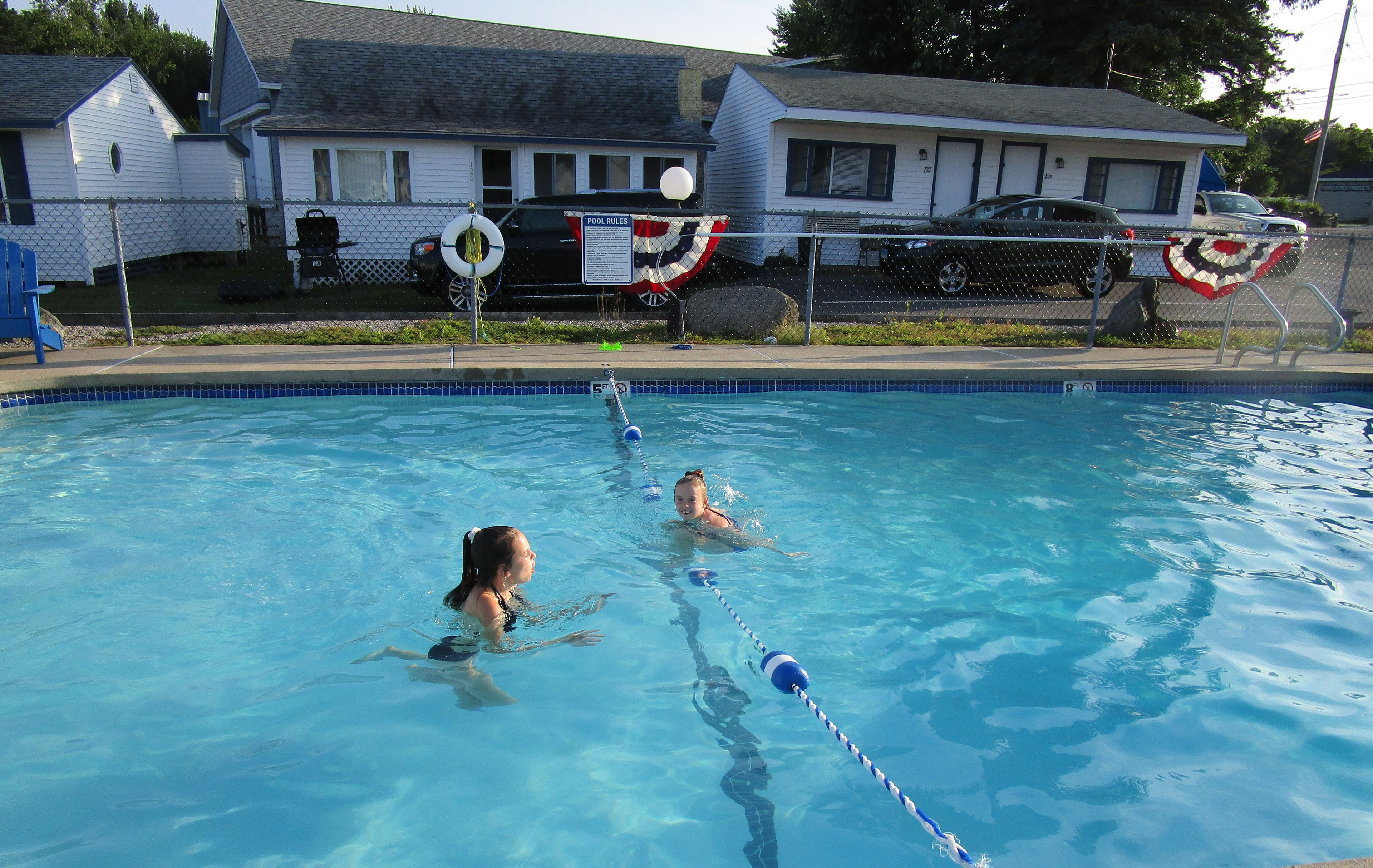 Une piscine à l’eau d’un bleu limpide, entourée d’une clôture en treillis métallique.
