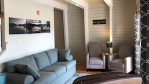 Una sala de estar acogedora con un sofá gris, dos sillones, una mesita auxiliar con una lámpara y un cartel en la pared que dice 'Green Cape Cottage'.
