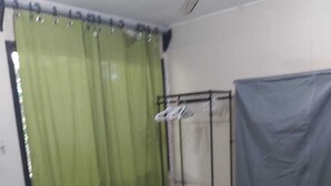 Een slaapkamer met een bed, een stoel, een plafondventilator, een gordijn en een metalen rek.