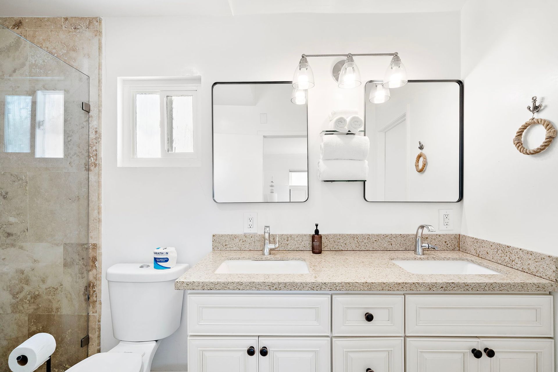A bathroom with a double sink, a toilet, a shower area, and a large mirror with lights.