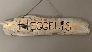 Ein rustikales Holzschild mit dem Schriftzug "HEGGELIS", das an einer Wand hängt.