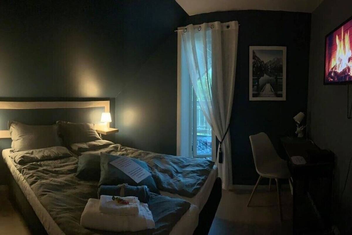 A bedroom with a bed, bedside lamps, a chair, a desk, a TV, and a window with curtains.