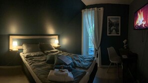 A bedroom with a bed, bedside lamps, a chair, a desk, a TV, and a window with curtains.