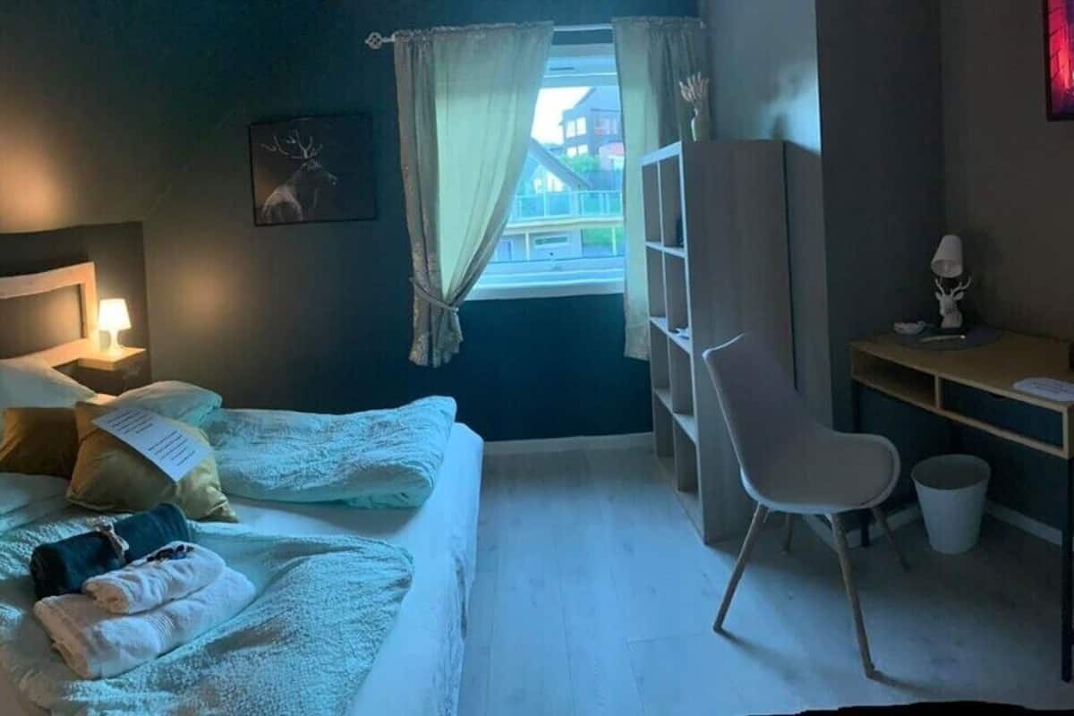 A bedroom with a bed, bedside table, lamp, and a desk with a chair.