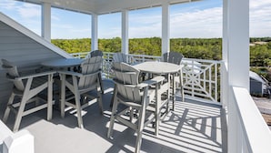 A covered outdoor seating area with a table and chairs, overlooking a lush landscape.