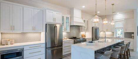 A modern kitchen with white cabinets, stainless steel appliances, and a central island with bar stools.