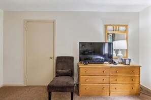 Una habitación de hotel con una cama individual, televisión, cómoda, silla y puerta.
