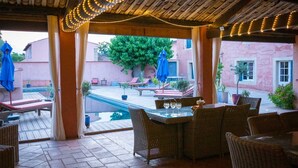 An outdoor patio with wicker furniture, a pool, and string lights. - Le Mas De Gleyzes (Ledenon)