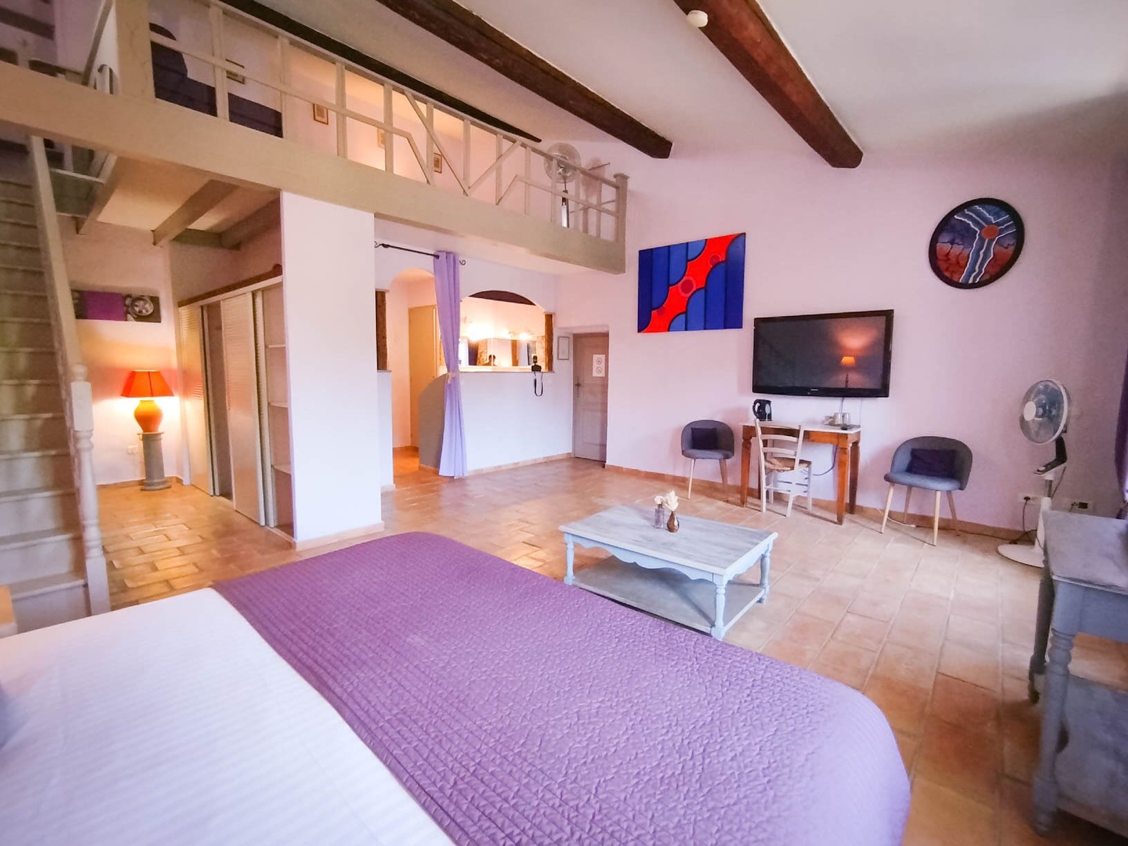 Una habitación amplia con cama, escritorio, silla, televisión y balcón.