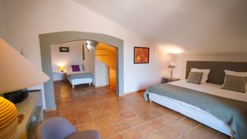 A bedroom with a bed, a chair, a desk, and a bathroom visible through an archway.