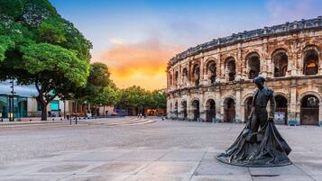 Une place où se trouve un bâtiment historique, caractérisé par de nombreuses arcades et une statue en premier plan.
