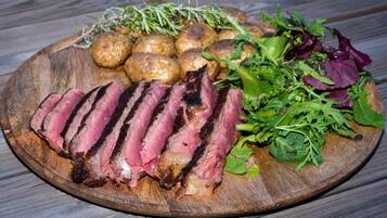 A wooden board with sliced steak, roasted potatoes, and mixed greens.