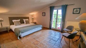 Un dormitorio con cama, mesitas de noche, una silla, una mesa y vistas al exterior a través de una ventana.