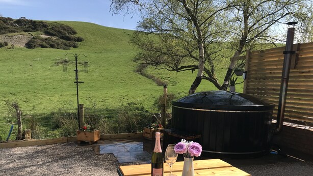 An outdoor seating area with a table, a bottle of champagne, and a vase of flowers. - Countryside Home with jacuzzi hot tub, open plan living and wood burner. (Ruthin)