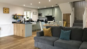 A modern kitchen with light-colored cabinets, a central island, and a dining area with a table and chairs. - Countryside Home with jacuzzi hot tub, open plan living and wood burner. (Ruthin)