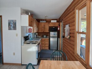 Eine kleine Küche mit Holzwänden, einem Herd, einem Kühlschrank und einem Essbereich mit Tisch und Stühlen.