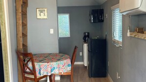 A compact kitchen with a dining table, chairs, a refrigerator, and a microwave. - The GREEN Tiny House (Houston)