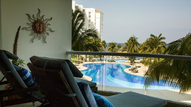Un balcón con sillones de mimbre y vistas a una piscina y palmeras.