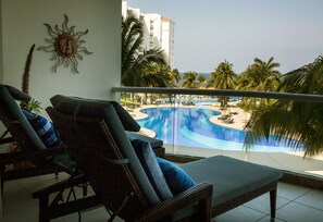 Ein Balkon mit Korlounge-Möbeln und Blick auf Pool und Palmen.